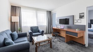 Een hotelkamer met een bank, een bureau met een computer, een televisie en een raam met gordijnen.