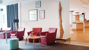 Een hal met rode zitplaatsen, een houten bijzettafeltje en kunstwerken in lijsten aan de muur.