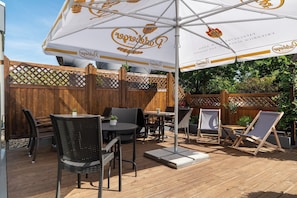 Eine Terrasse im Freien mit Holzmöbeln, einem großen Sonnenschirm und einem Holzzaun.