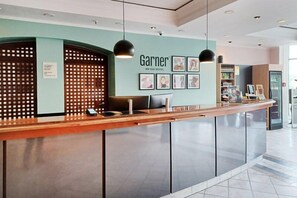 A hotel reception desk with a modern design, a name sign, and a seating area. - Select Hotel Russelsheim (Ruesselsheim)