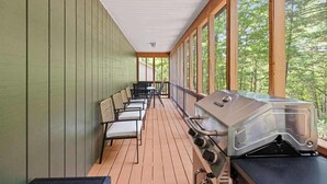 Ein überdachter Außenbereich mit Grill, Sitzgelegenheiten und großen Fenstern.