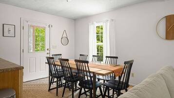A dining area with a wooden table and black chairs, white walls, and windows with curtains.