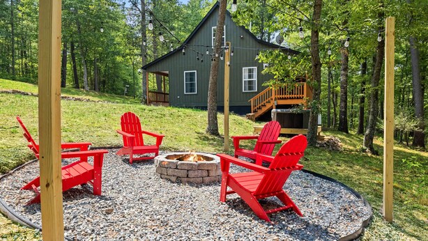 Eine Hütte mit einer Terrasse, umgeben von einem Kiesplatz mit roten Adirondack-Stühlen und einer Feuerstelle.