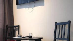 A small room with a single table and two chairs, a flat-screen TV mounted on the wall, and a curtain partially covering a window. - North West Hotel & Restaurant (Hvammstangi)