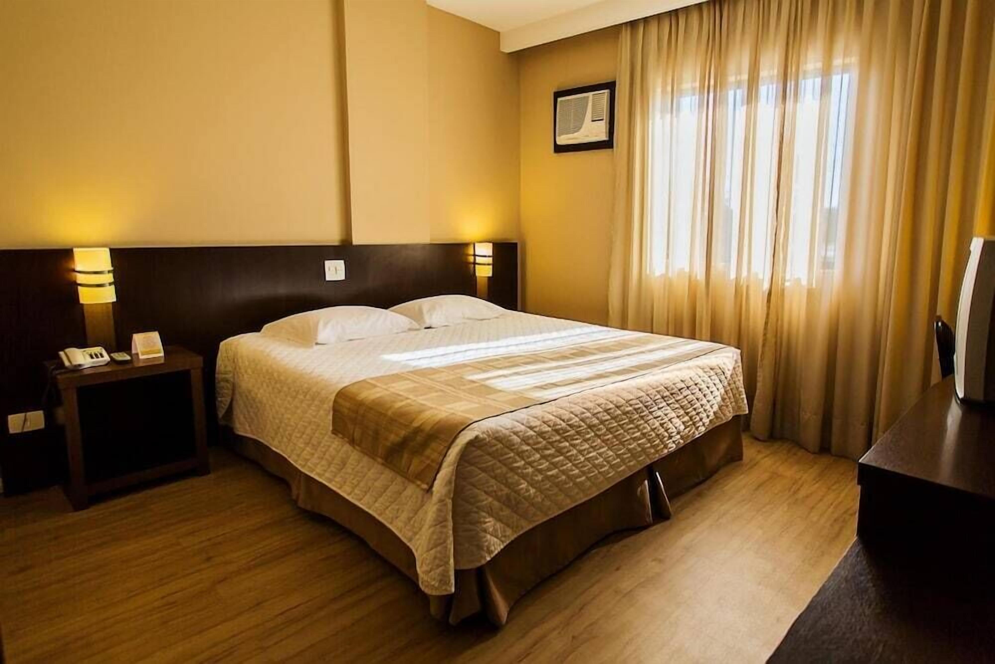 A hotel room with a large bed, bedside lamps, a nightstand with a phone, and a window with curtains.