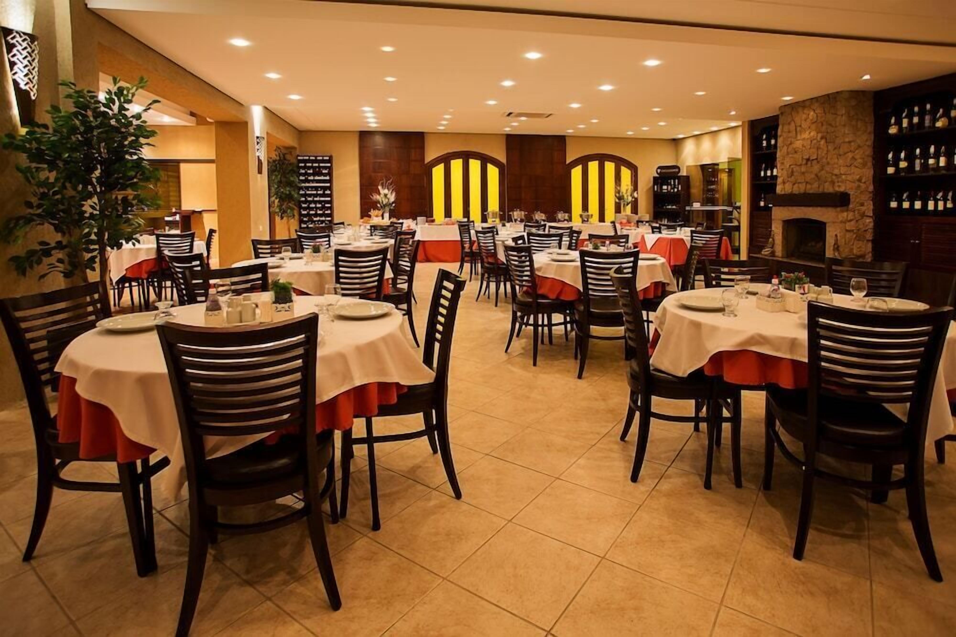 A restaurant with round tables, black chairs, and a stone fireplace.