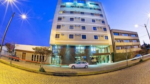 A multi-story hotel with a modern design, featuring a prominent entrance and a visible car parked in front. - Hotel Campo Largo (Campo Largo)