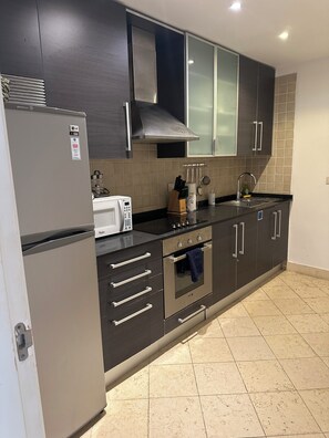 Eine moderne Küche mit dunklen Schränken, einem Edelstahl-Kühlschrank, einer Mikrowelle und einem Gasherd.