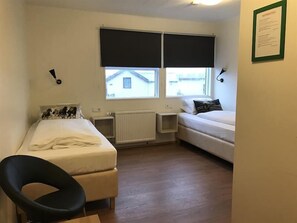 Een kleine, net kamer met twee bedden, een stoel en een radiator.