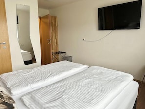 Een hotelkamer met een bed, een aan de muur bevestigde televisie en een houten garderobe.