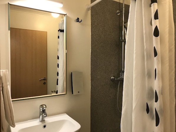 Ein Badezimmer mit Waschbecken, Spiegel, Dusche und Handtuchhalter.
