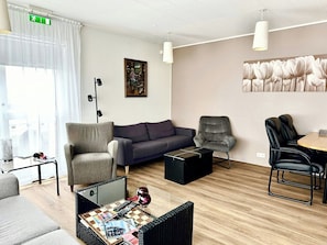 A modern hotel room with a grey sofa, a grey armchair, a black coffee table, and a small table with a chessboard.