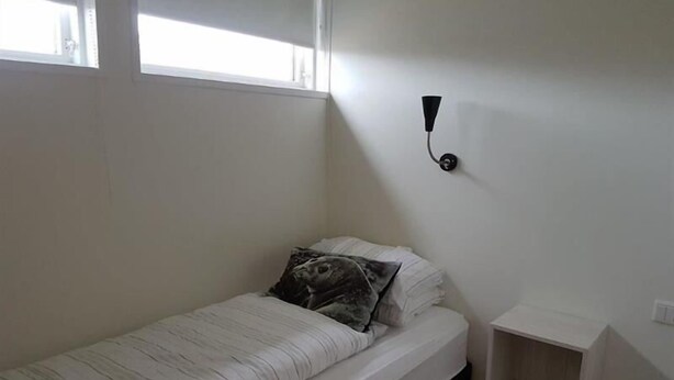 A small, single-bed room with a white bed, a nightstand, and a wall-mounted light fixture. - Hotel Hvammstangi (Hvammstangi)