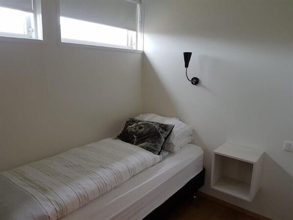 Een kleine kamer met een eenpersoonsbed, een nachtkastje en een wandlamp.