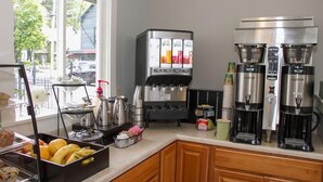A kitchen with a fruit display, coffee machines, and a coffee station. - Bar Harbor Villager Motel (Bar Harbor)
