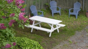 A picnic table with four blue Adirondack chairs and pink flowers in the background. - Bar Harbor Villager Motel (Bar Harbor)