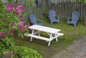 Una mesa de picnic con cuatro sillas Adirondack azules y flores rosadas al fondo.