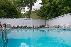 Una piscina con sillas de descanso blancas y una valla blanca.