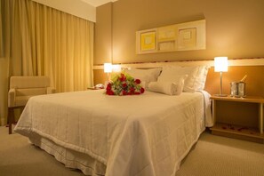 Ein Hotelzimmer mit einem großen Bett, zwei Nachttischlampen, einem Sessel und einem Nachttisch mit Lampe und Glas.