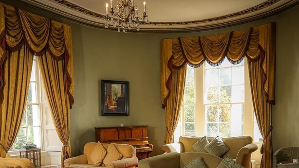 A spacious living room with a grand chandelier, multiple sofas, a piano, and large windows with curtains. - Springfort Hall Hotel (Mallow)