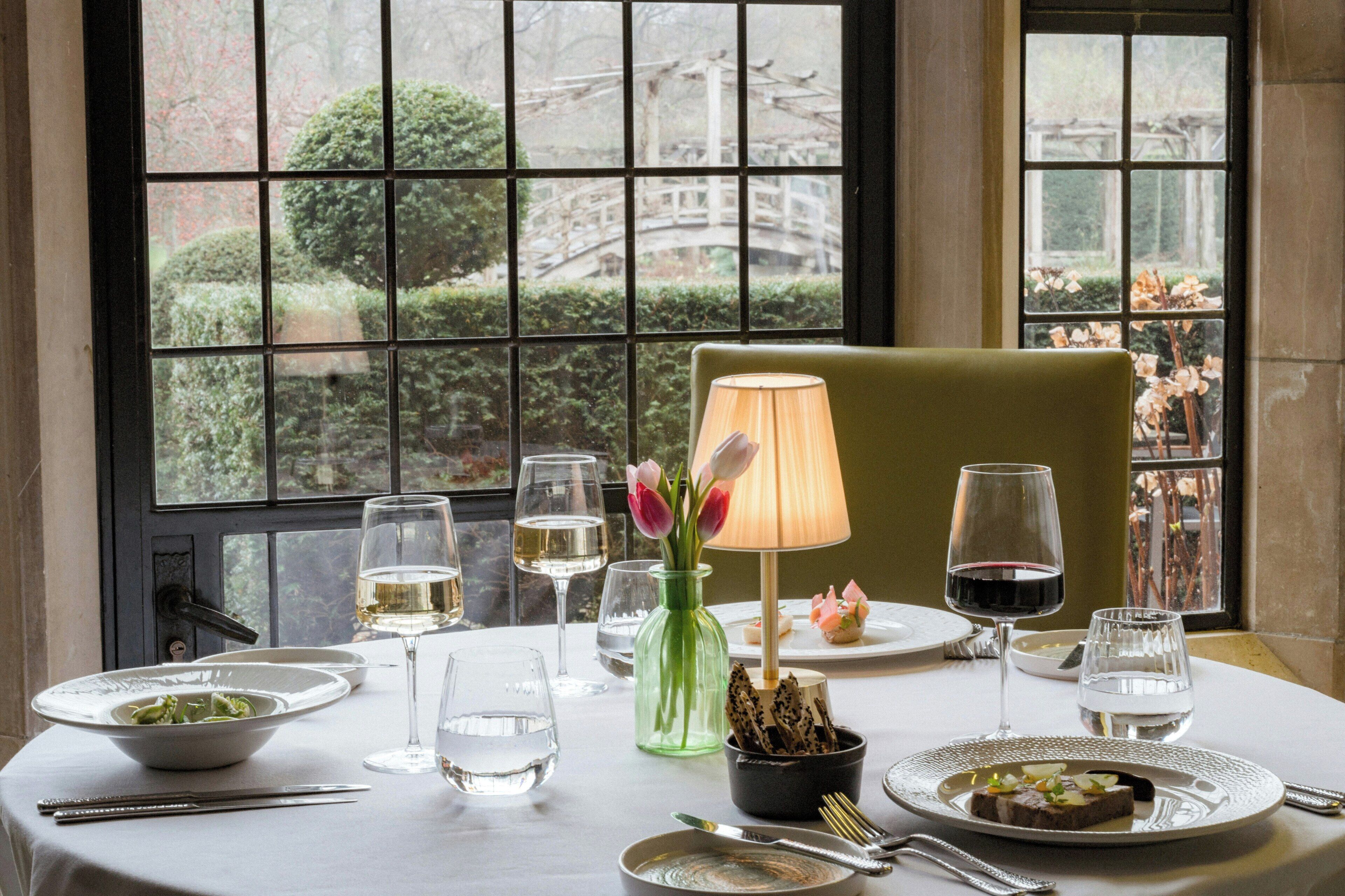 A dining table set with plates, glasses, cutlery, a vase with flowers, and a lamp.