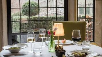 A dining table set with plates, glasses, cutlery, a vase with flowers, and a lamp.