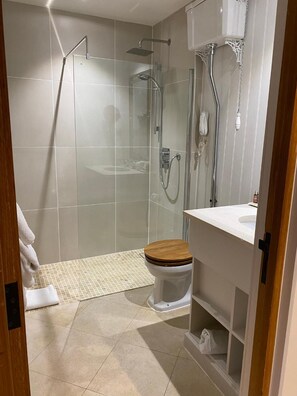 A modern bathroom with a glass-enclosed shower, a wooden toilet, and a white sink. - Great Fosters (Egham)