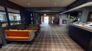 A hotel lobby with a check-in counter, seating area with orange sofas, and a check-in desk. - Village Manchester Hyde Hotel Leisure Club (Hyde)