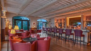 A bar area with red upholstered chairs, a bar counter, and a wooden ceiling. - Coquillade Village (Gargas)