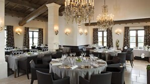 A dining area with round tables set for a meal, chandeliers, and wall sconces. - Coquillade Village (Gargas)
