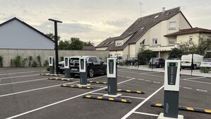 A parking area with electric vehicle charging stations, marked parking spaces, and a building in the background. - Brit Hotel Le Relais du Ried (Bischwihr)