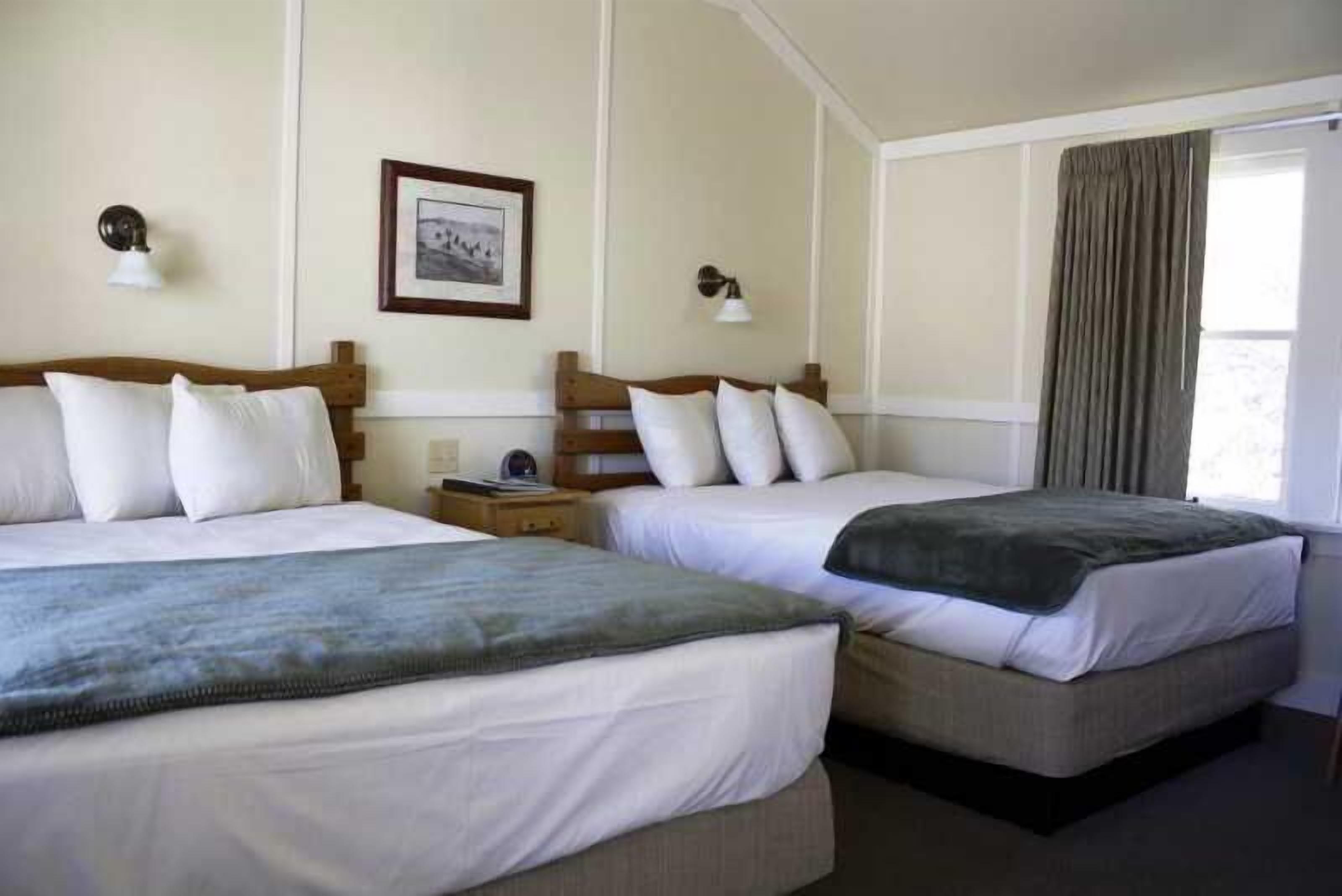 A hotel room with two beds, a framed picture on the wall, and a window with curtains.