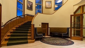 A grand staircase with wooden railings and carpeted steps, leading to a landing with a large, ornate mirror and a round, patterned rug. - Mammoth Hot Springs (Yellowstone National Park)