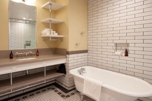 A bathroom with a white bathtub, two sinks, a mirror, and a tiled wall.