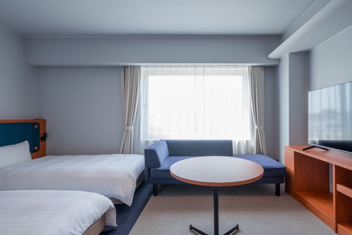 Ett hotellrum med två sängar, en soffa, ett litet runt bord och en tv.