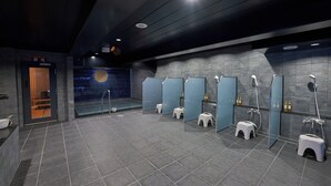 Une salle de bain moderne avec des carreaux gris, plusieurs lavabos et une douche à l’italienne en verre.