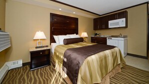 Habitación de hotel con cama, dos mesitas de noche con lámparas, microondas, kitchenette y piso alfombrado.