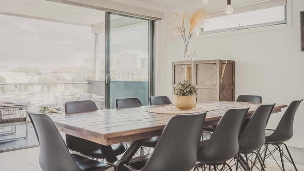 A modern dining area with a wooden table and black chairs, large windows, and a view of the city.