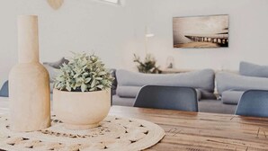 A dining table with a wooden vase and a potted plant, a grey sofa, and a framed picture on the wall.