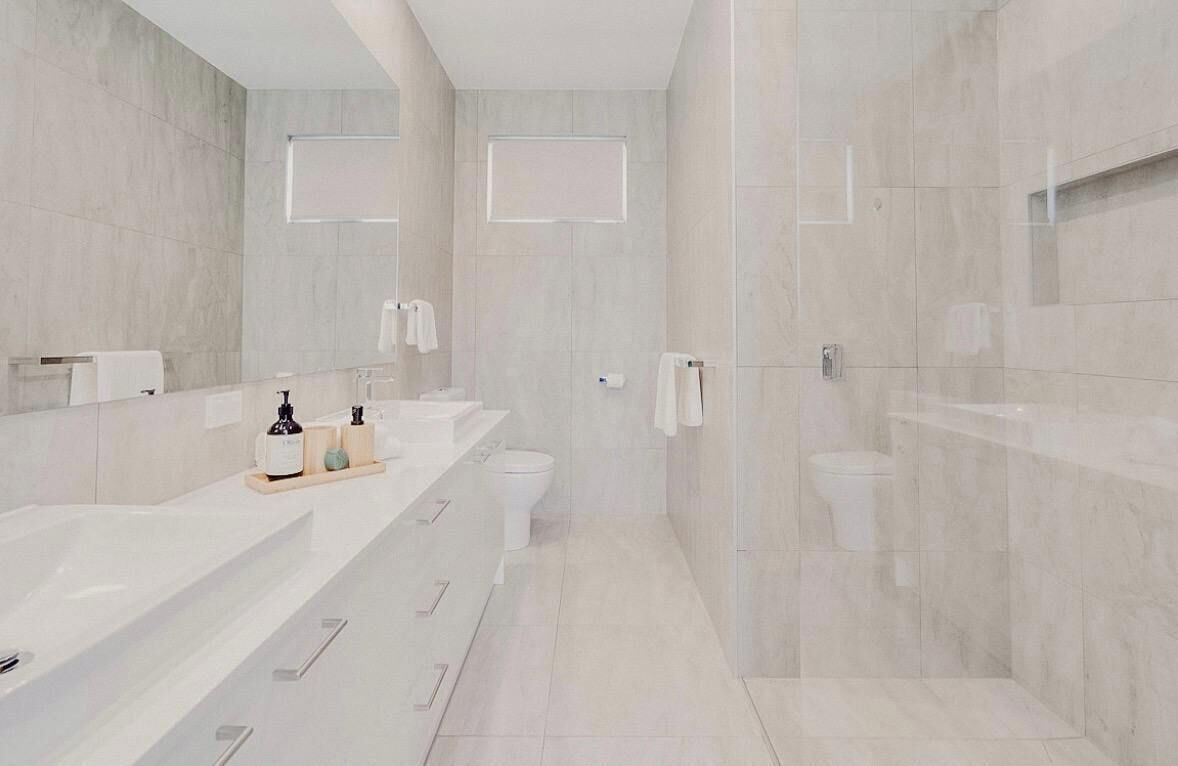 A modern bathroom with a large mirror, a white sink, a toilet, and a shower area.