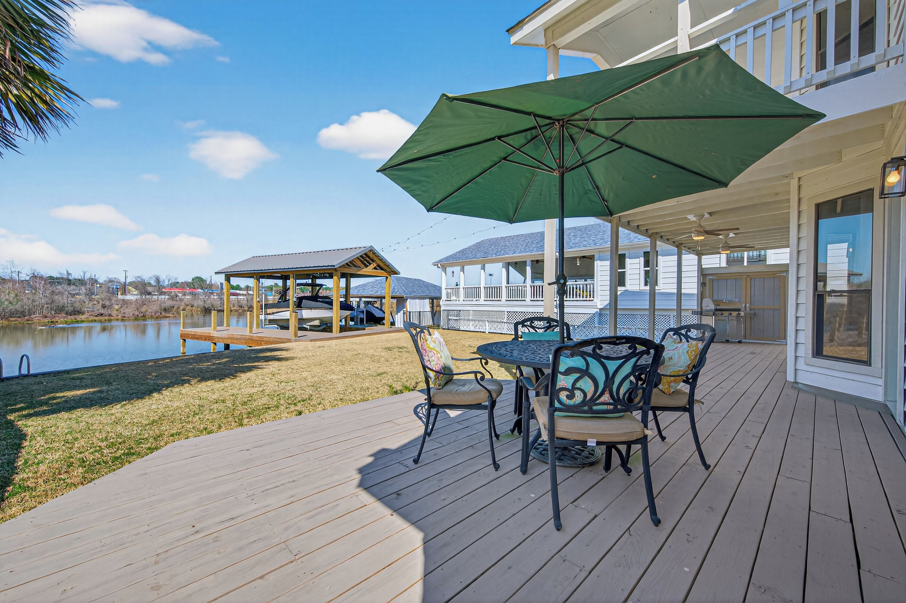 A wooden deck with outdoor furniture, a green umbrella, and a view of a lake and buildings in the background.