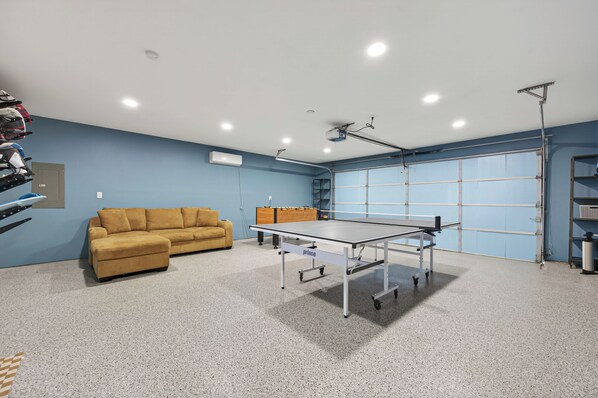 Habitació amb taula de ping-pong, sofà, ventilador de sostre i porta de garatge.