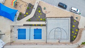 Eine Vogelperspektive auf eine Sportanlage mit Basketballfeld, Tennisplatz und einem Spielbereich.