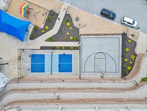 Eine Vogelperspektive auf eine Sportanlage mit Basketballfeld, Tennisplatz und einem Spielbereich.