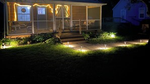 A house with a covered porch, outdoor seating, and a well-lit entrance. - Crabapple Cottage (Essex)