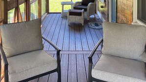 A covered porch with wooden beams, two chairs, a small table, and a ceiling fan. - Crabapple Cottage (Essex)