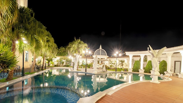 A nighttime swimming pool with a wooden deck, palm trees, and a gazebo. - Vela Luxury Hai Ha Hotel  (Quang Ha)