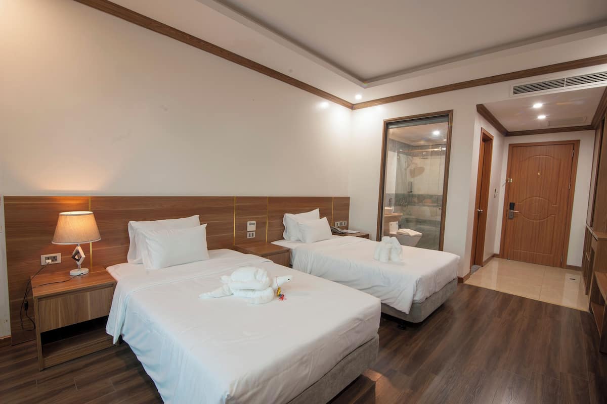 A hotel room with two beds, a wooden headboard, a nightstand with a lamp, and a mirror on the wall.