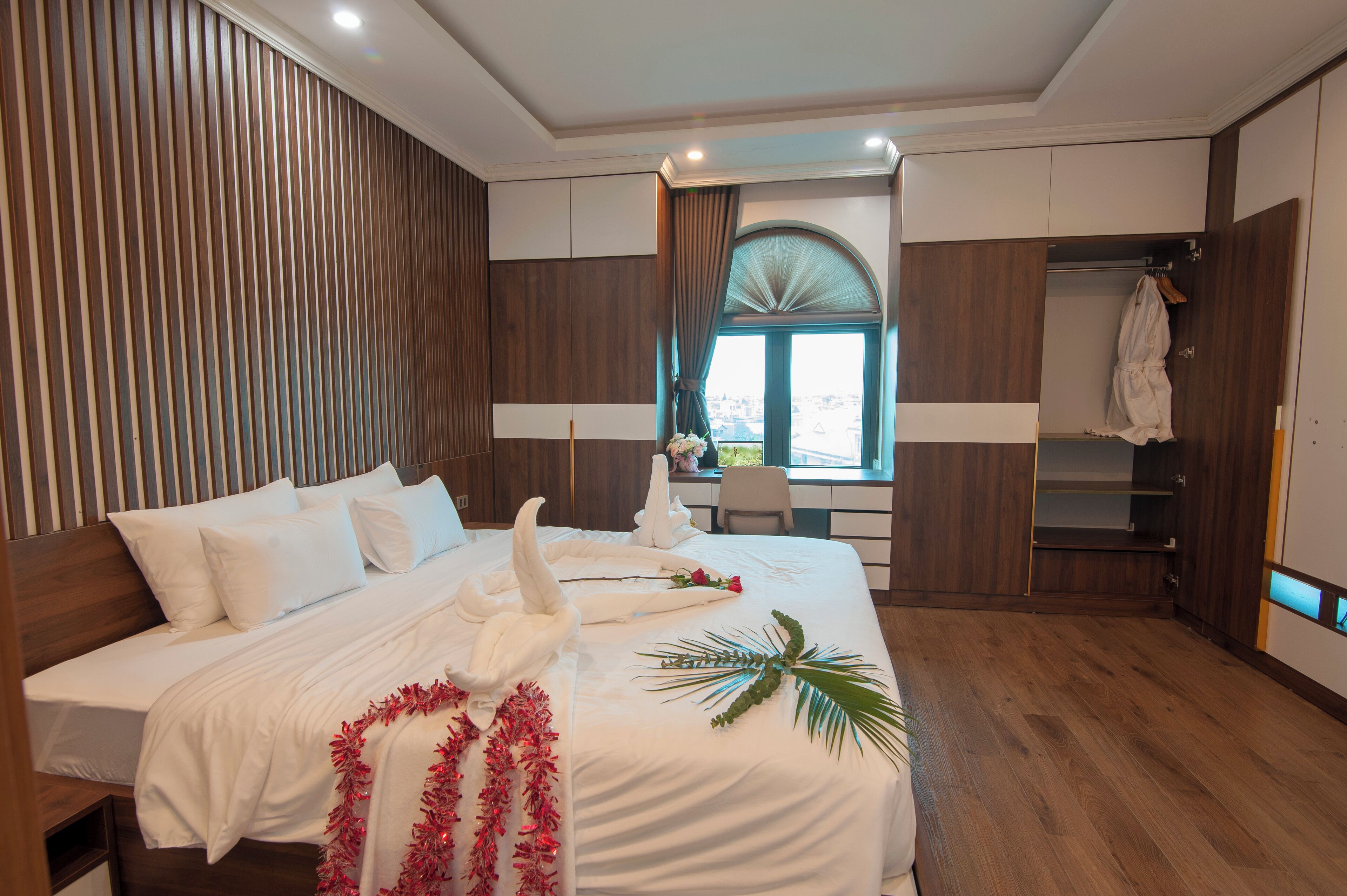 A hotel room with a large bed, wooden paneling, a desk, and a view through a window.