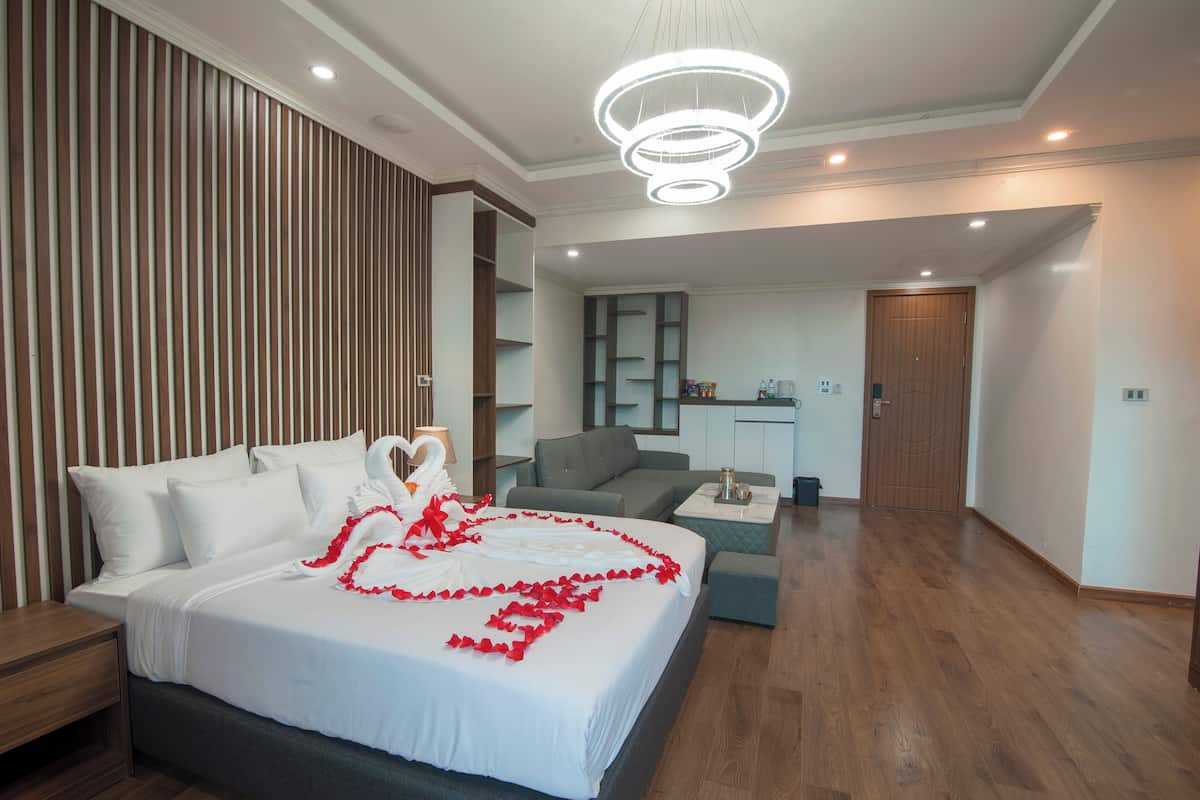 A modern hotel room with a large bed, a grey sofa, and a wooden wardrobe.